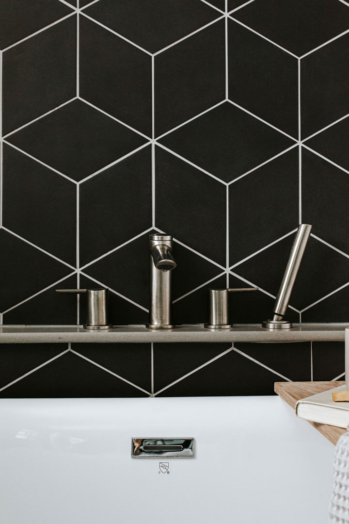 Modern and sleek brushed bathtub hardware on a wall of geometric tile design by Jennifer Murphy