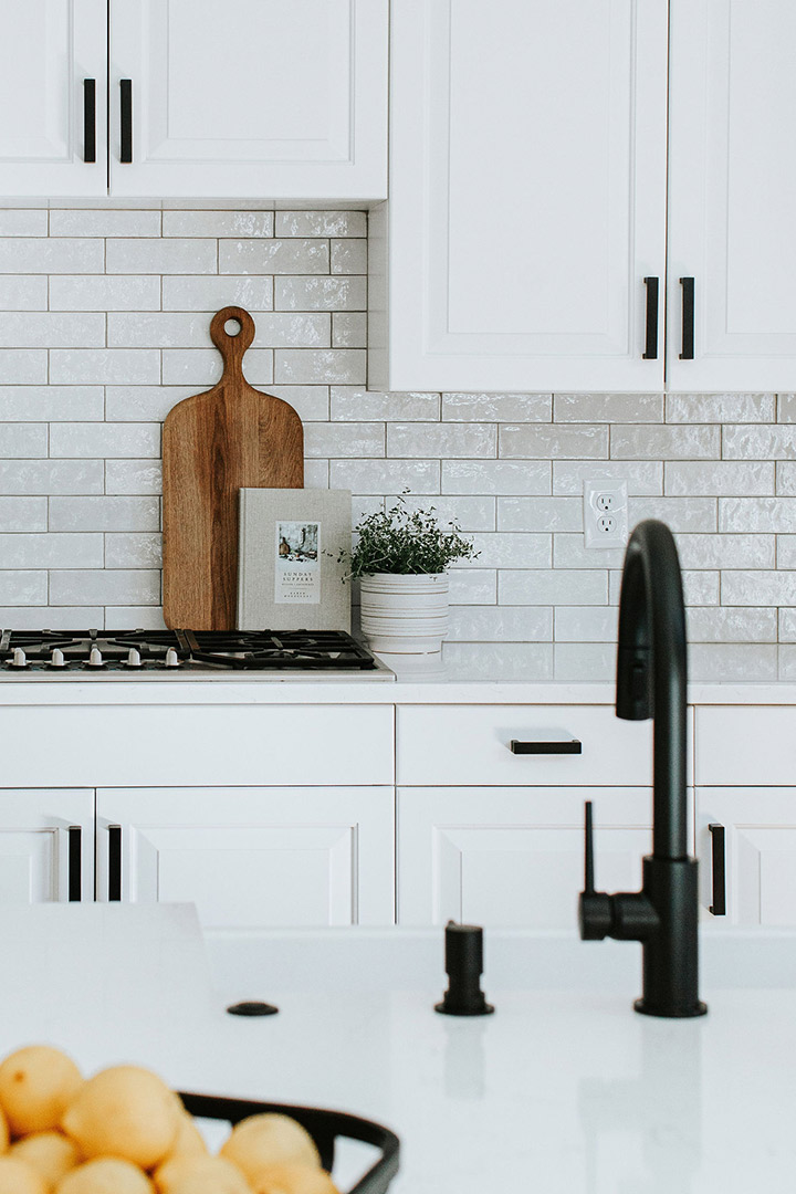 A beautifully textured thin white subway tile is sandwiched by bright white cabinets with black hardware.