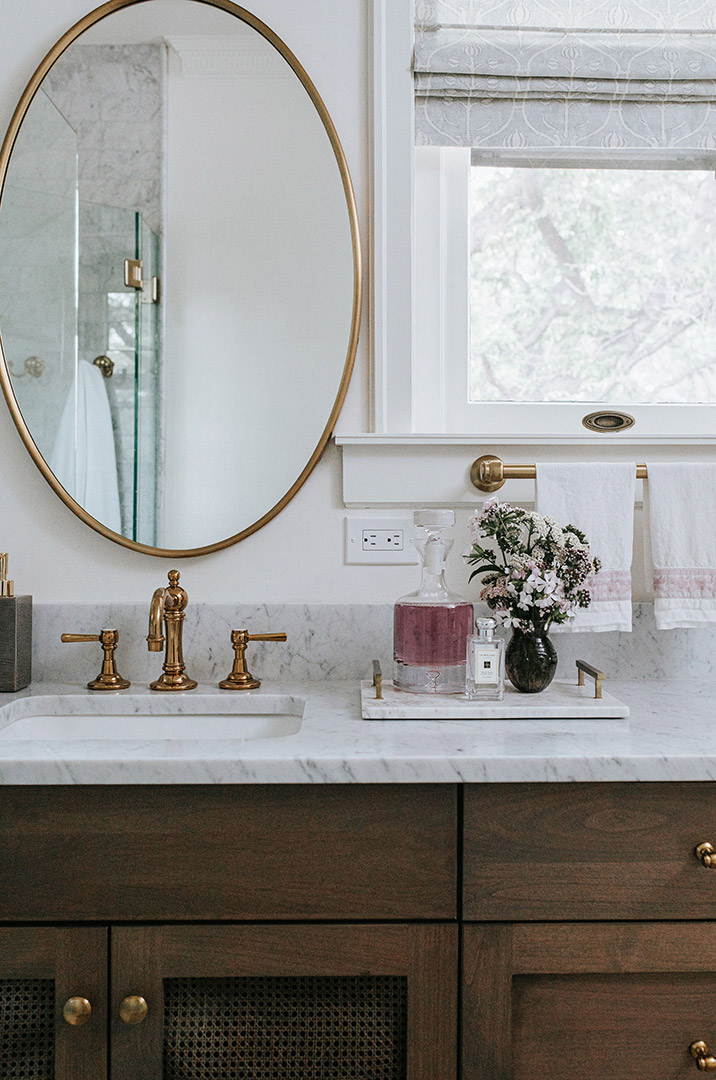 Dark stained cabinets with cane doors base the master bathrooms vanity, J.Reiko Design +  Co chose vintage inspired brass fixtures that make the traditional feel truly come to life. 