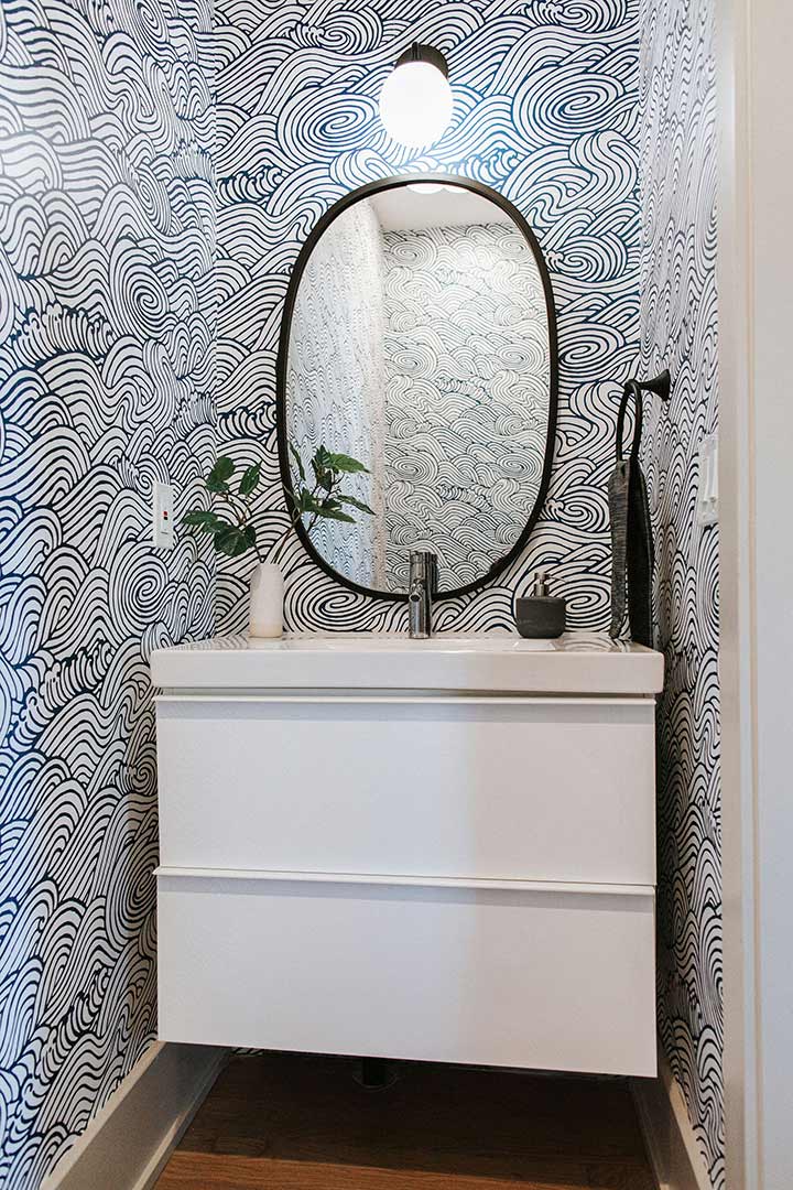 Modern wallpaper with a navy and white wave pattern wrap around a clean white floating vanity with black fixtures in this modern bathroom renovation in Denver, Colorado.