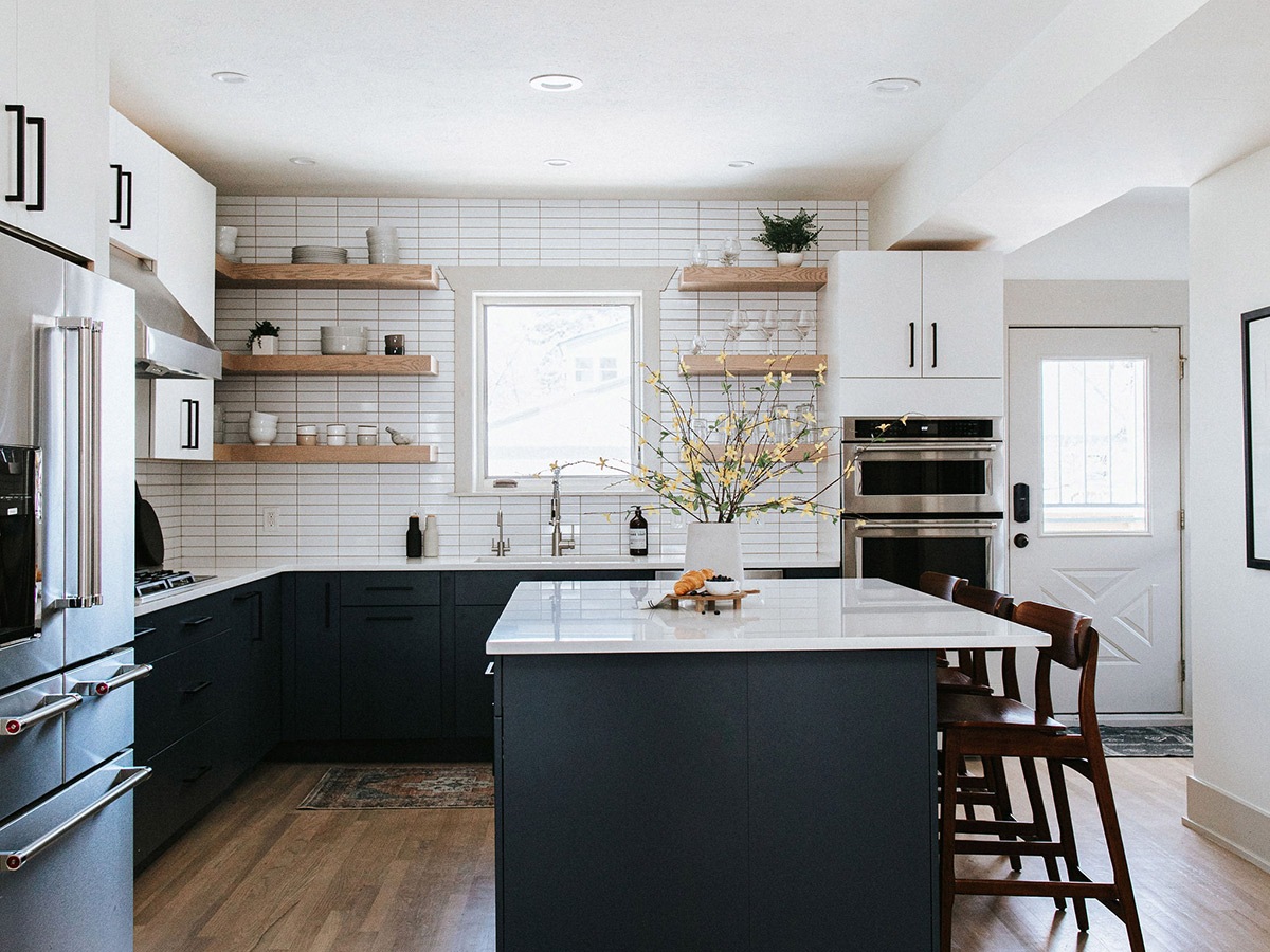 Natural wood barstools accent the white oak flooring of this kitchen renovation with bright white cabinets and navy island. 