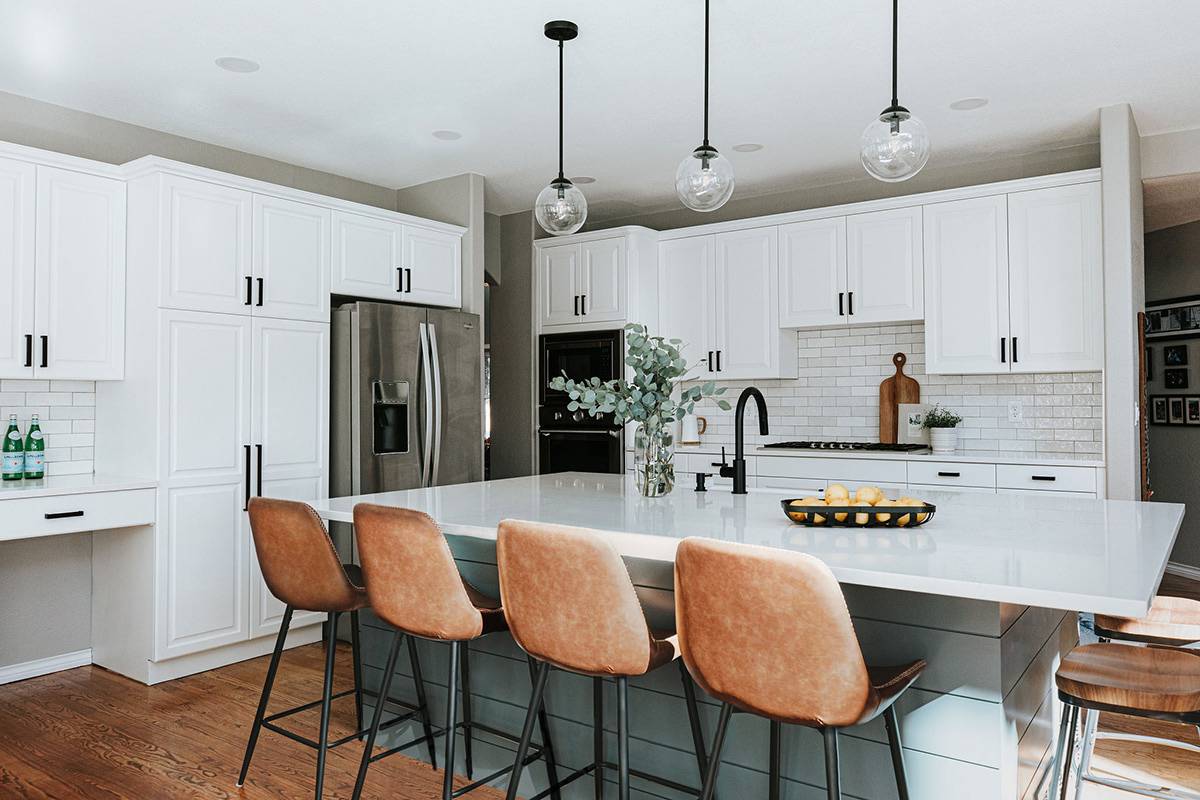 Leather barstools steal the show of this kitchen renovation with bright white cabinets and a teal shiplap island. 