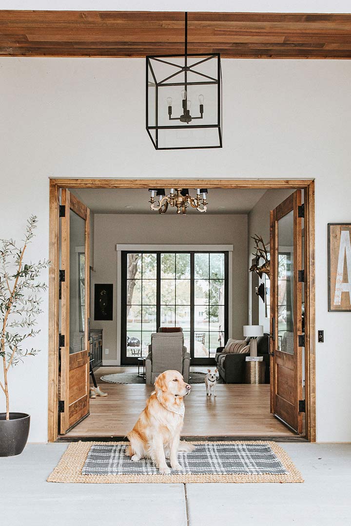 Front doors of the entry of this modern farmhouse home are open while the family's golden retriever sits in front on a welcome mat