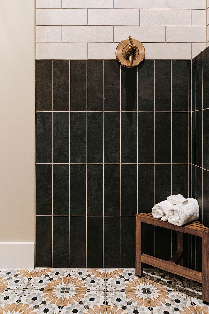 Patterned tile of the base of this shower show a brass faucet.