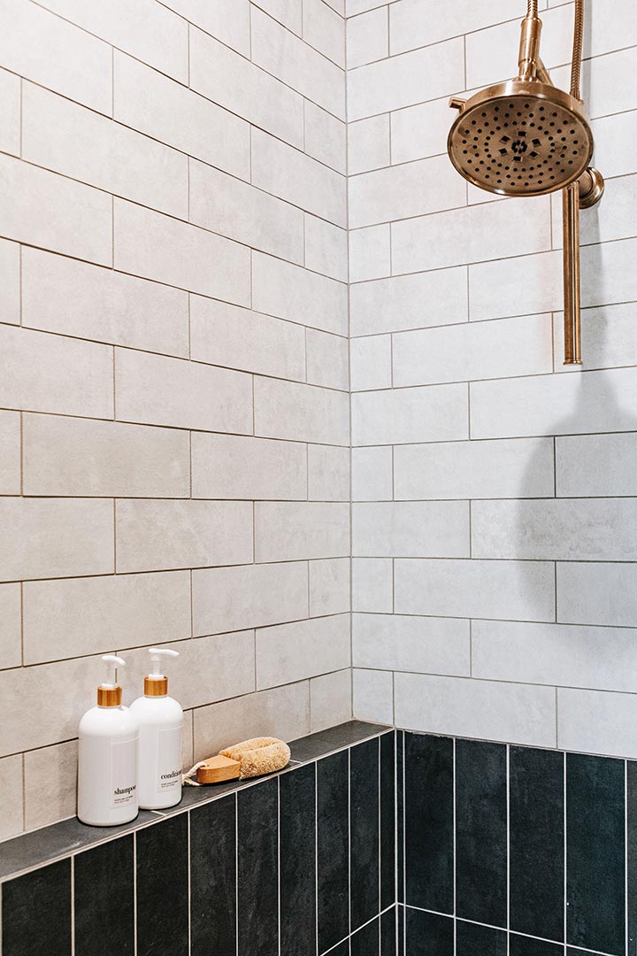 Two tone shower tile and brass shower head hardware in a modern interior design hallway bath