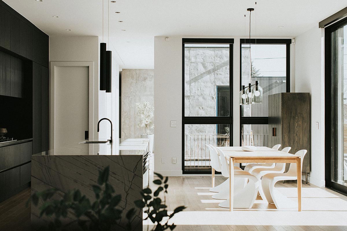 A beautiful and dramatic image showcasing the balance between dark and light in this minimalist kitchen with rich darks to the left and bright light pouring in the window to the right.