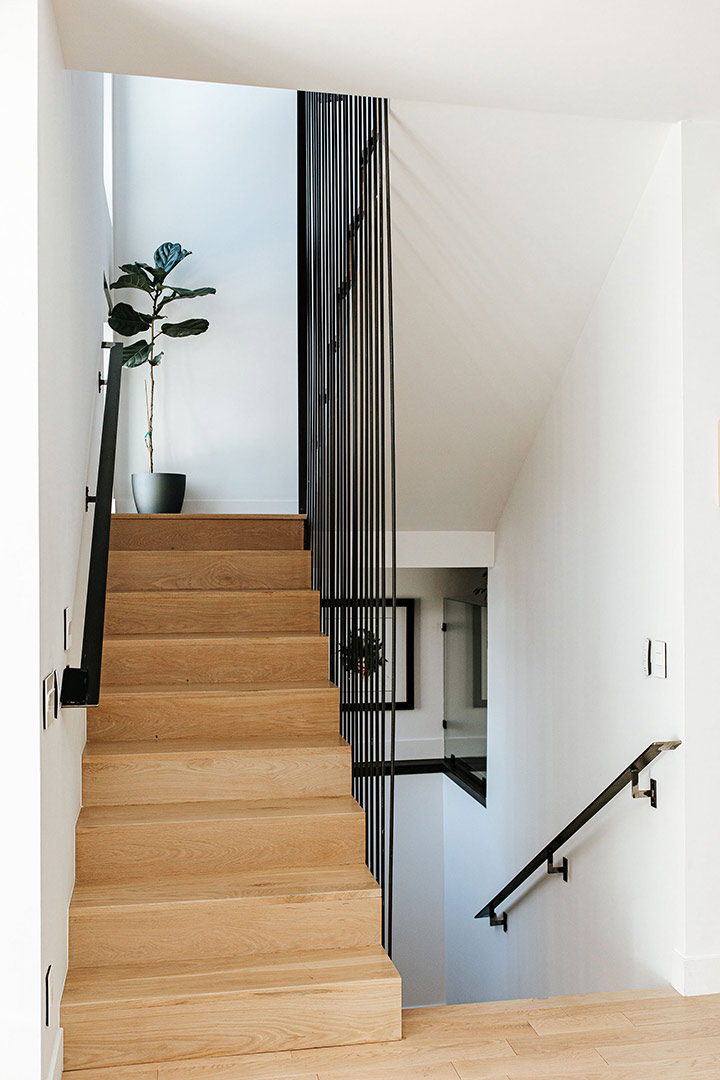 A custom metal railing with vertical black bars frame white oak treads and risers giving this Denver new build home a contemporary feel. 