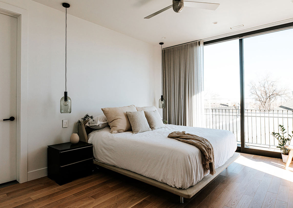 A Scandinavian bedroom design by J. Reiko Design + Co includes a contemporary platform bed with pendant lights hanging from the ceiling and a giant sliding glass door with a balcony that overlooks Denver's sunnyside neighborhood.