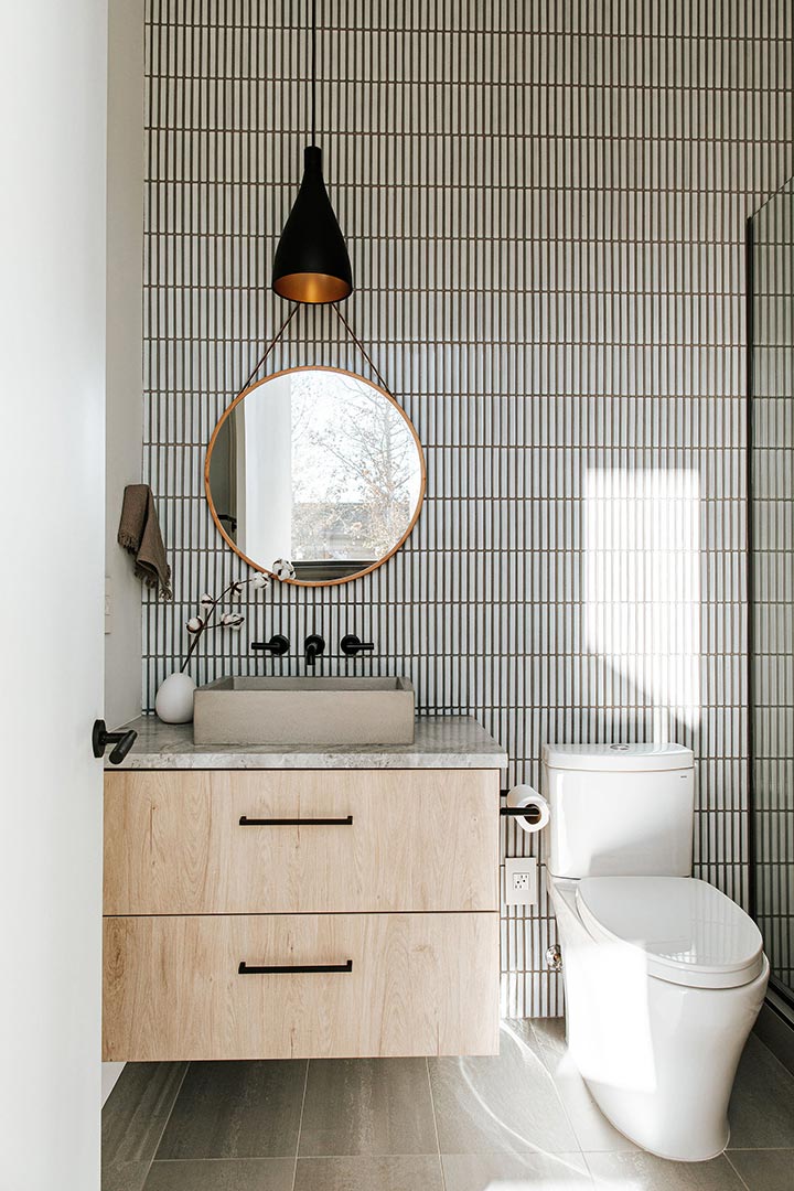 Tic-tac Zellige tile runs floor to ceiling in the view from the hallway paired with a white oak floating vanity with black fixtures and a gold circle mirror.