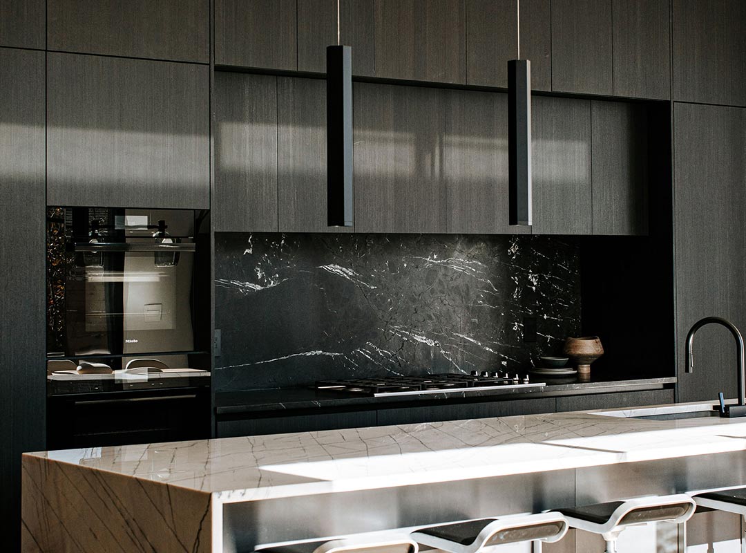 Rich black stained Shou Sugi Ban cabinets frame black marble with modern pendant lights and a waterfall marble island countertop paired perfectly by interior design and architecture firm J. Reiko + Co from Fort Collins Colorado.