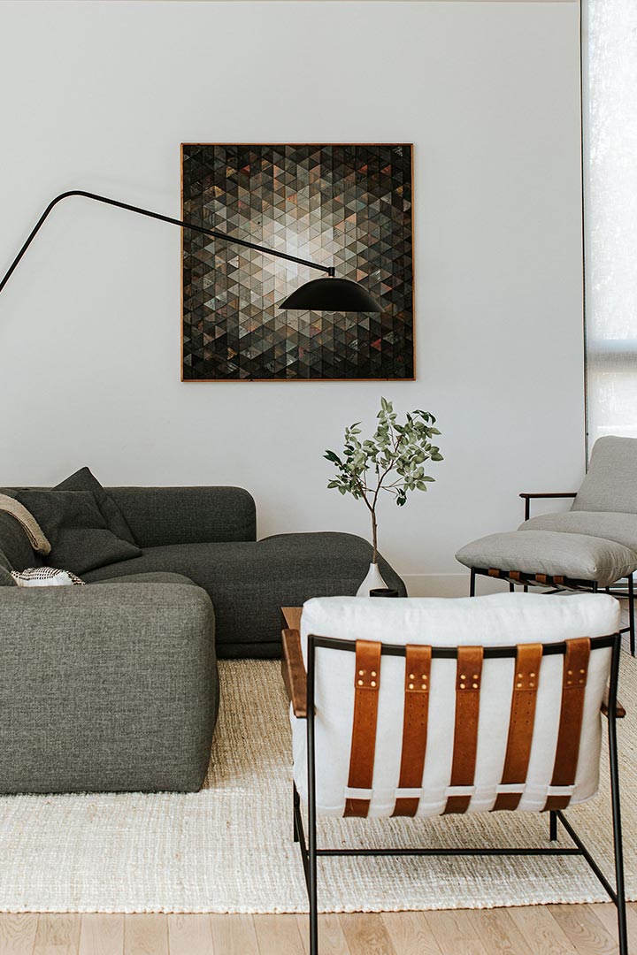 The leather straps on this Denver living room's modern chairs pair with the natural fiber rug and geometric artwork.