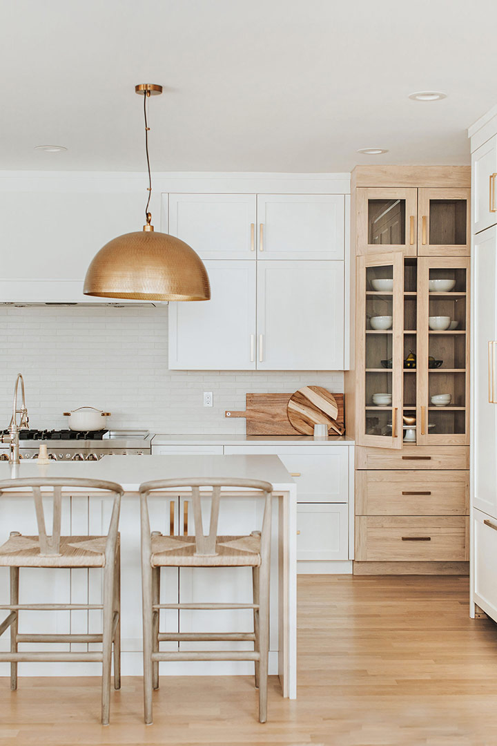 Natural wishbone backed barstools nestle under the white oak lined waterfall quartz countertop complimented by white oak floors and a white oak featured cabinet.