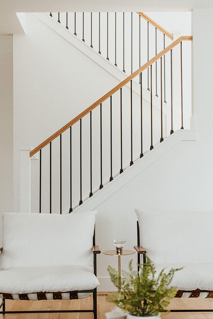 The back and forth zigzag of a modern staircase's white oak and black iron railings are featured above a modern pairing for leather strapped chairs.