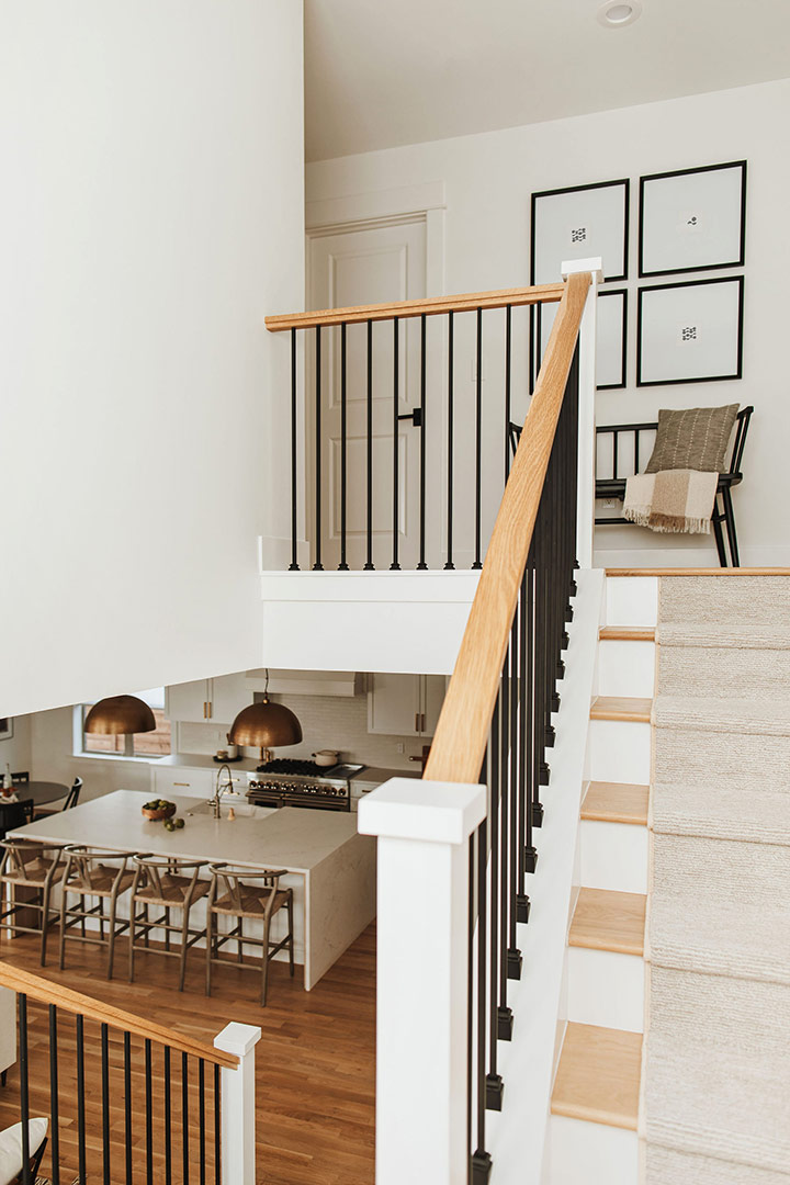 A view from the midway landing of this modern minimalist stairwell shows a view below into a modern kitchen and a view above onto a top landing with a cute modern farmhouse style bench
