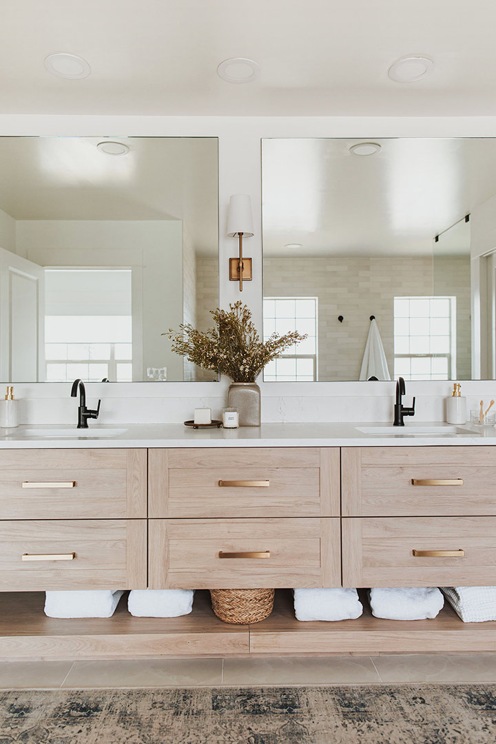 Modern white oak vanity with brass pulls and scones in a primary bath with double sinks with modern black faucets 