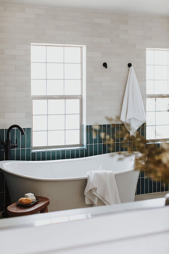 A view of the freestanding bath that is backed by Bedrosians Makoto Arashi Blue Wainscotting paired with horizontal Bedrosians Makoto Shoji White Wall Tile