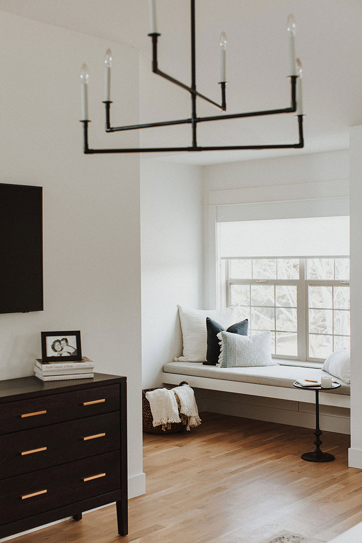 A modern aged iron chandelier frames the White Window Bench Seat in this Denver whole home renovation's primary bedroom