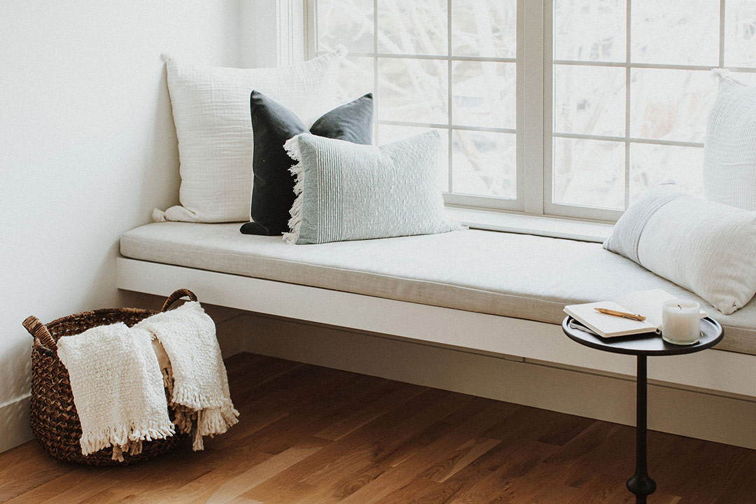 A modern built-in White Window Bench Seat with a side table and white oak floors with natural toned pillows 