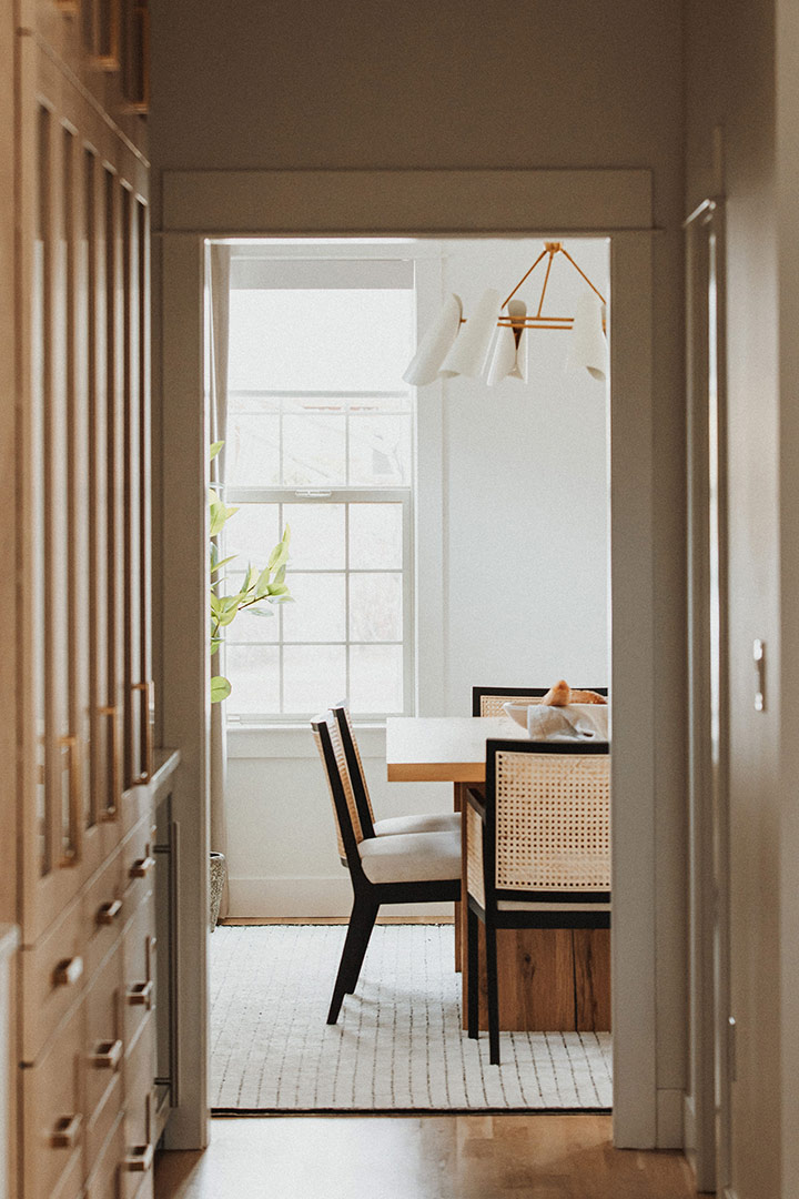 White oak cabinets in this modern kitchen renovation frame the doorway leading to the minimal dining room featuring caned back dining chairs paired perfectly by J. Reiko Design + Co