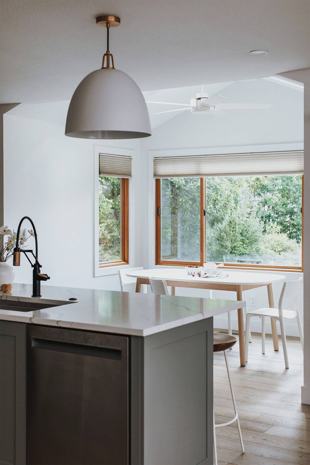 Oversized pendant light over a green cabinet island with quartz countertops over looking a minimalist scandinavian dining nook designed by J. Reiko Design + Co