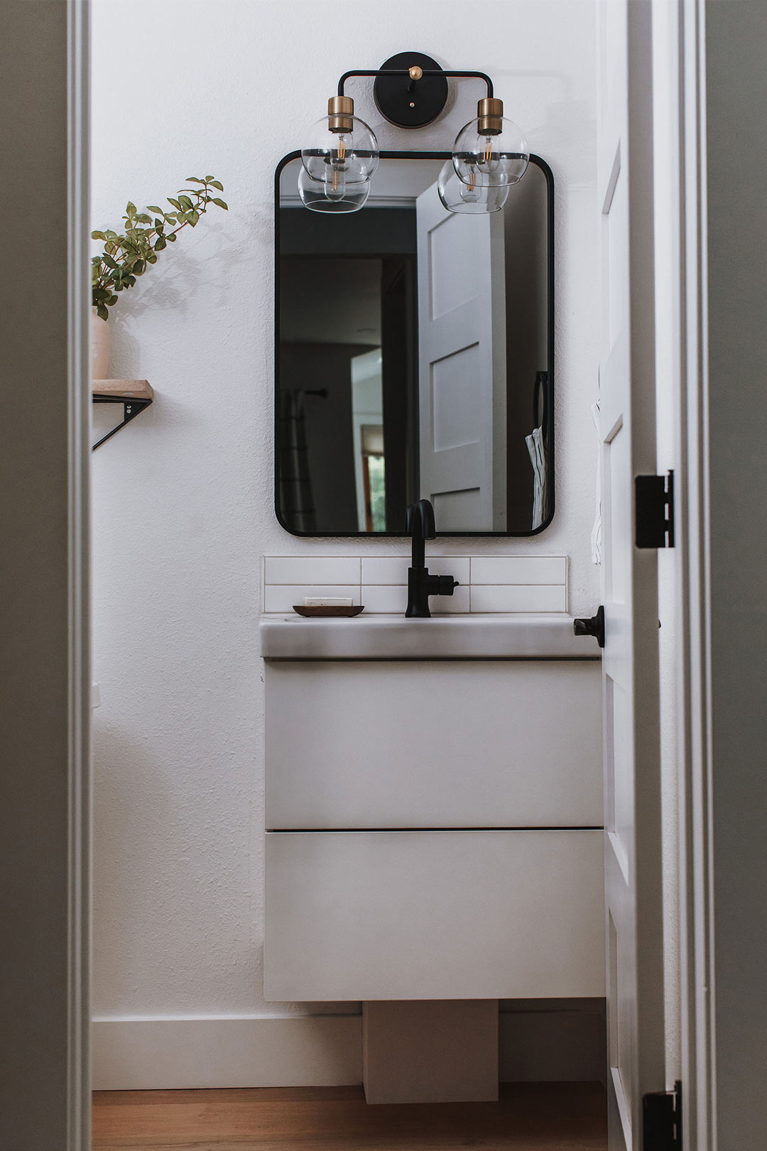 Modern Scandinavian bathroom with matte black faucet and mixed metal vanity light designed by J. Reiko Design + Co