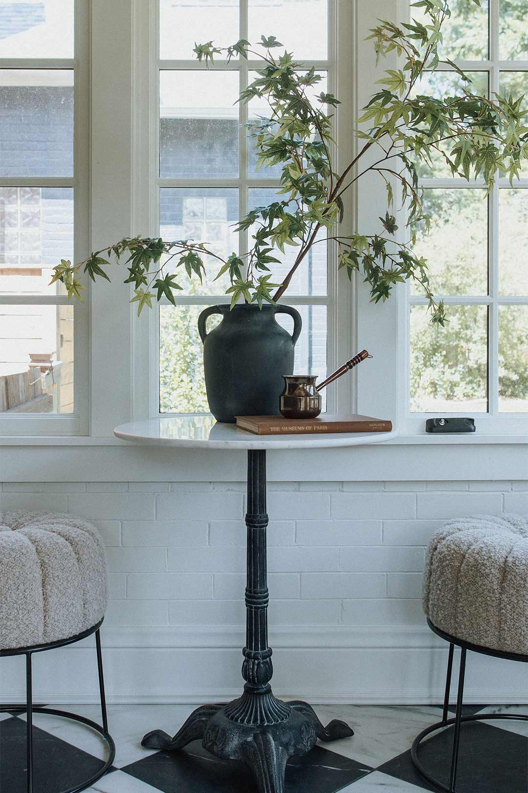 Marble bistro table with boucle pouf seating in a historic remodel's sunroom