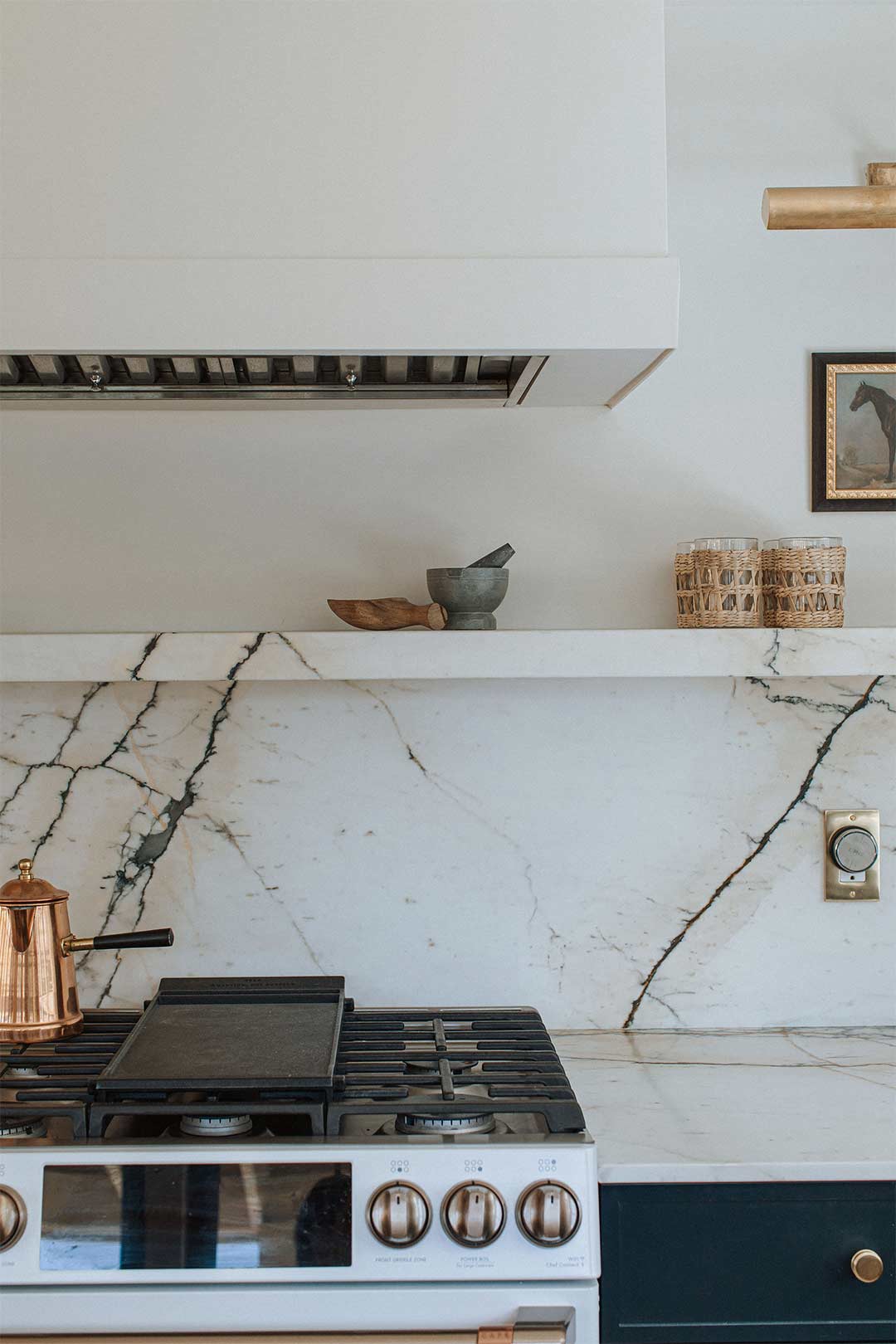 Marble backsplash with ledge on the range wall with brass fixtures and a white hood vent in a transitional designed kitchen in Denver Colorado.