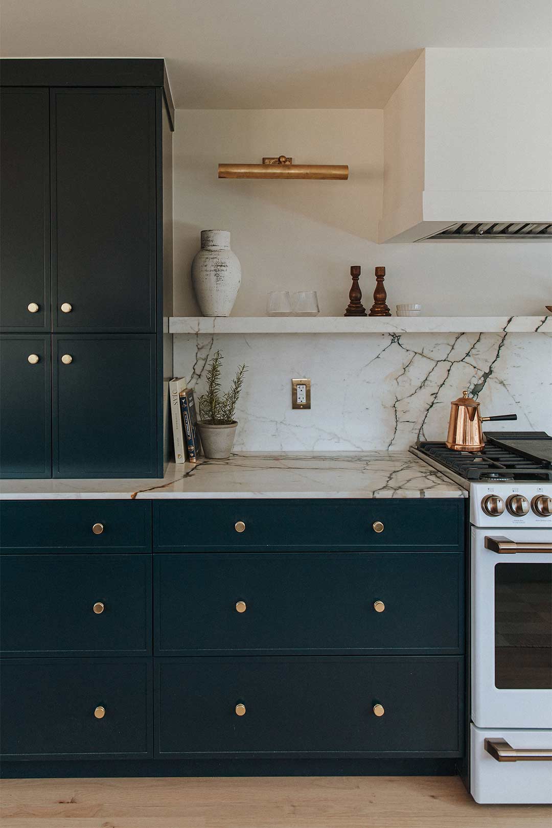 Blue cabinets with brass knobs and brass light fixture next to GE Cafe range in a historic Victorian house remodel