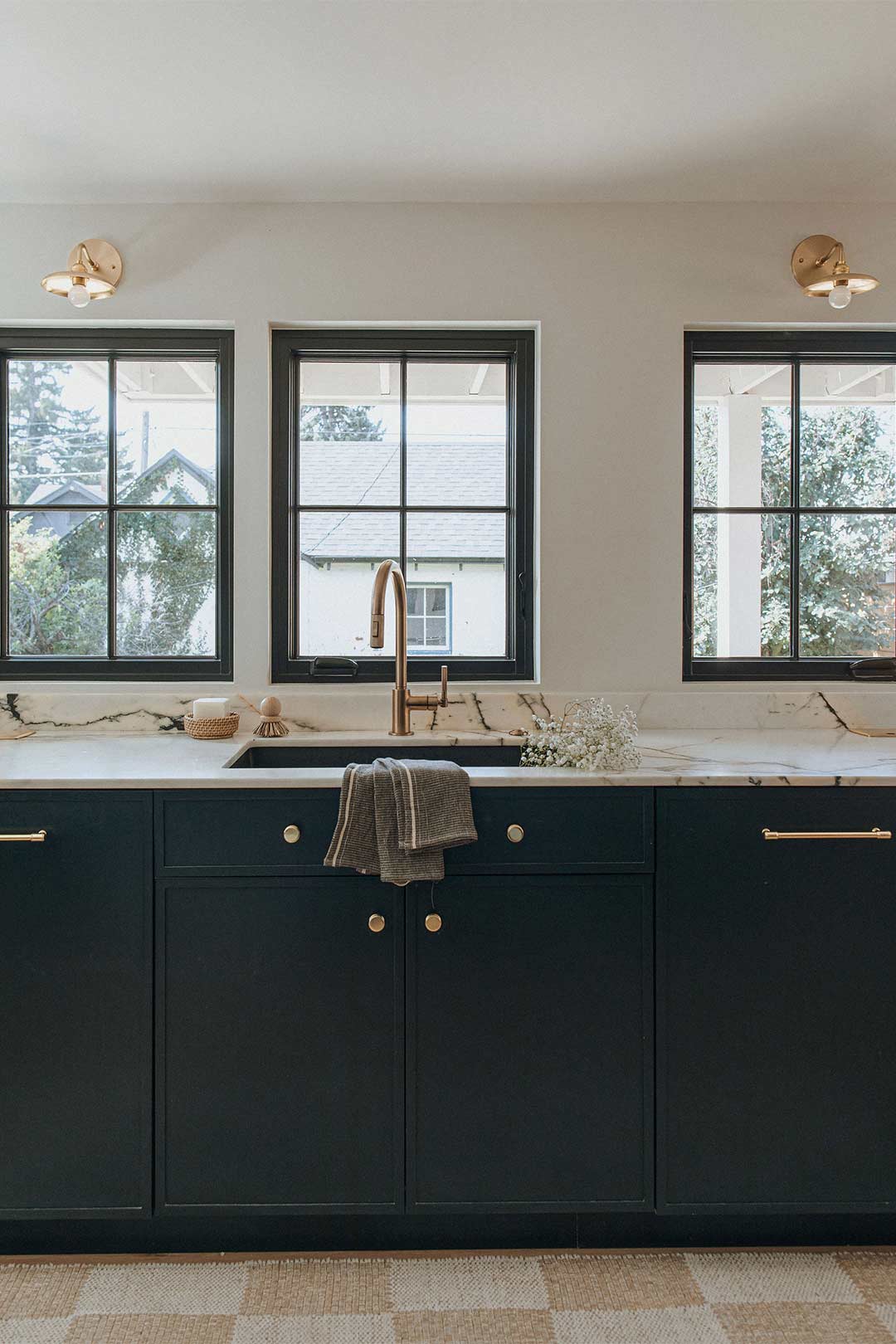 Traditional design kitchen sink with dark blue cabinets, brass knobs, brass faucet and brass light fixtues