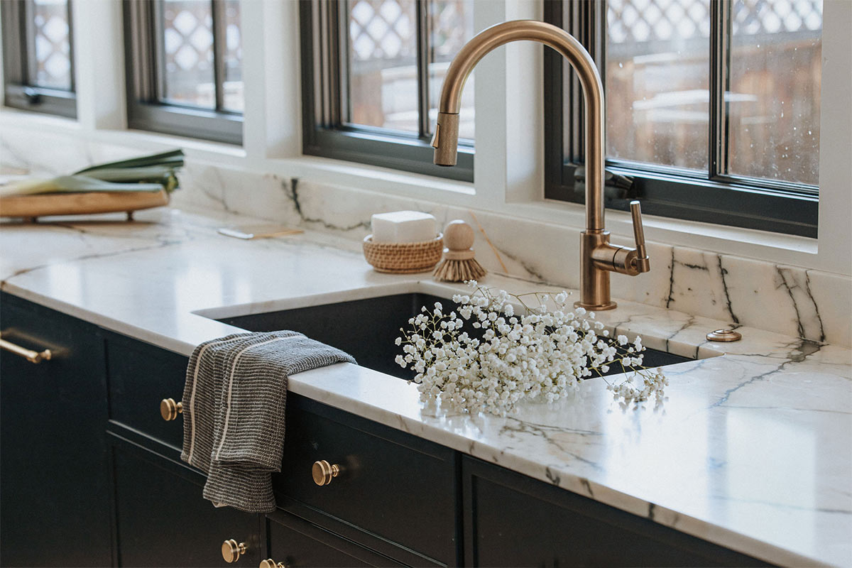 Brass brizo sink faucet paired with marble countertops and brass fixtures. 