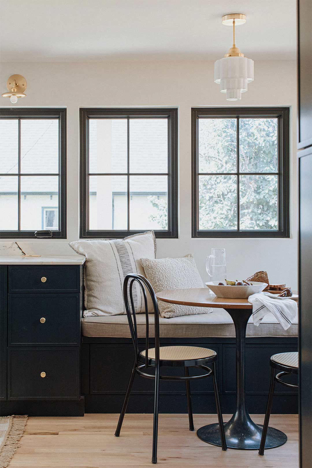 Historic remodel's dining nook with a dark blue bench seat brass pendant light overhead and black cane chairs styled by Jennifer Murphy of J. Reiko Design + Co