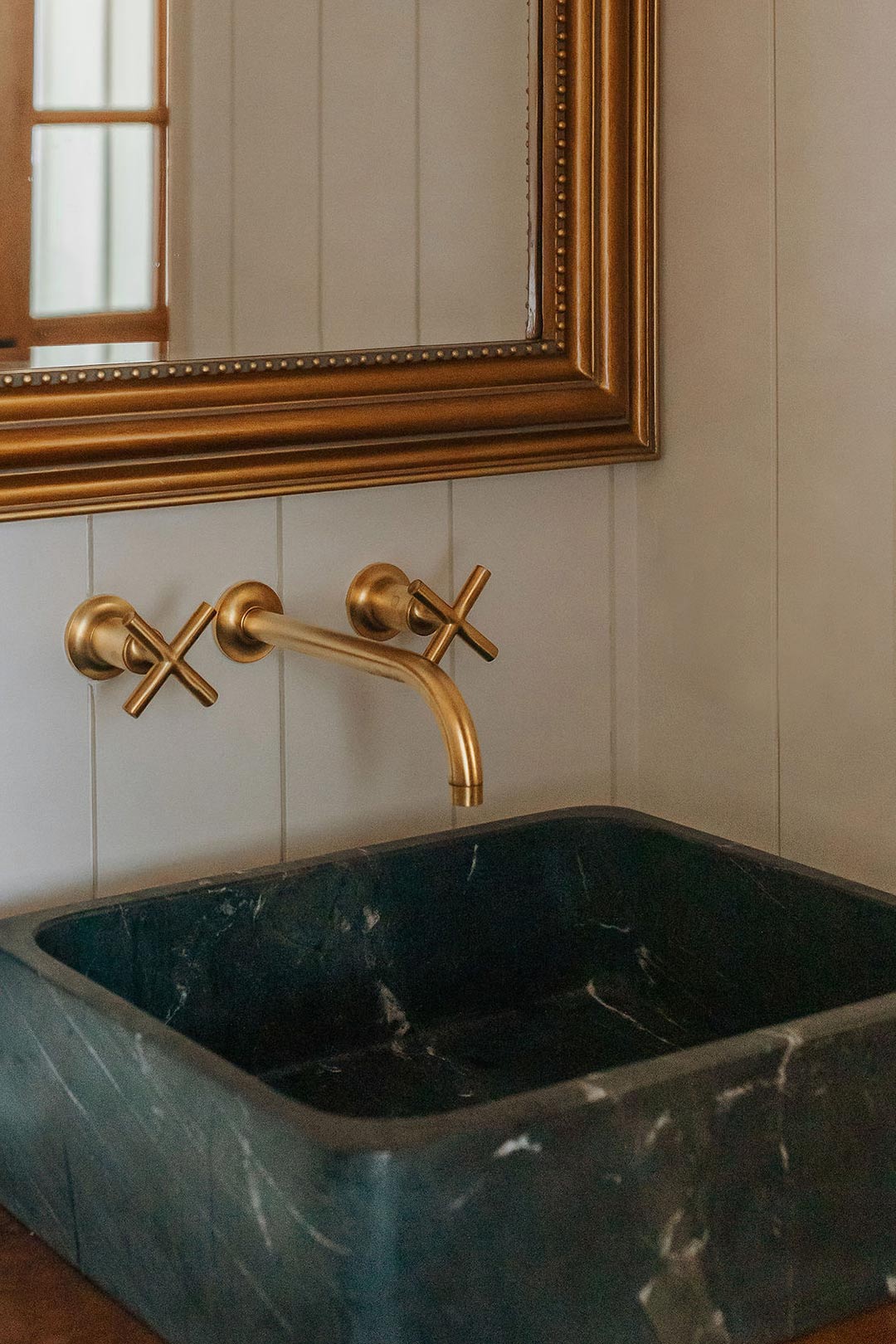 Kohler Purist Brass cross handle wall mount faucet paired with vintage inspired brass mirro and vertical shiplap wall paneling in a Modern farmhouse half bath