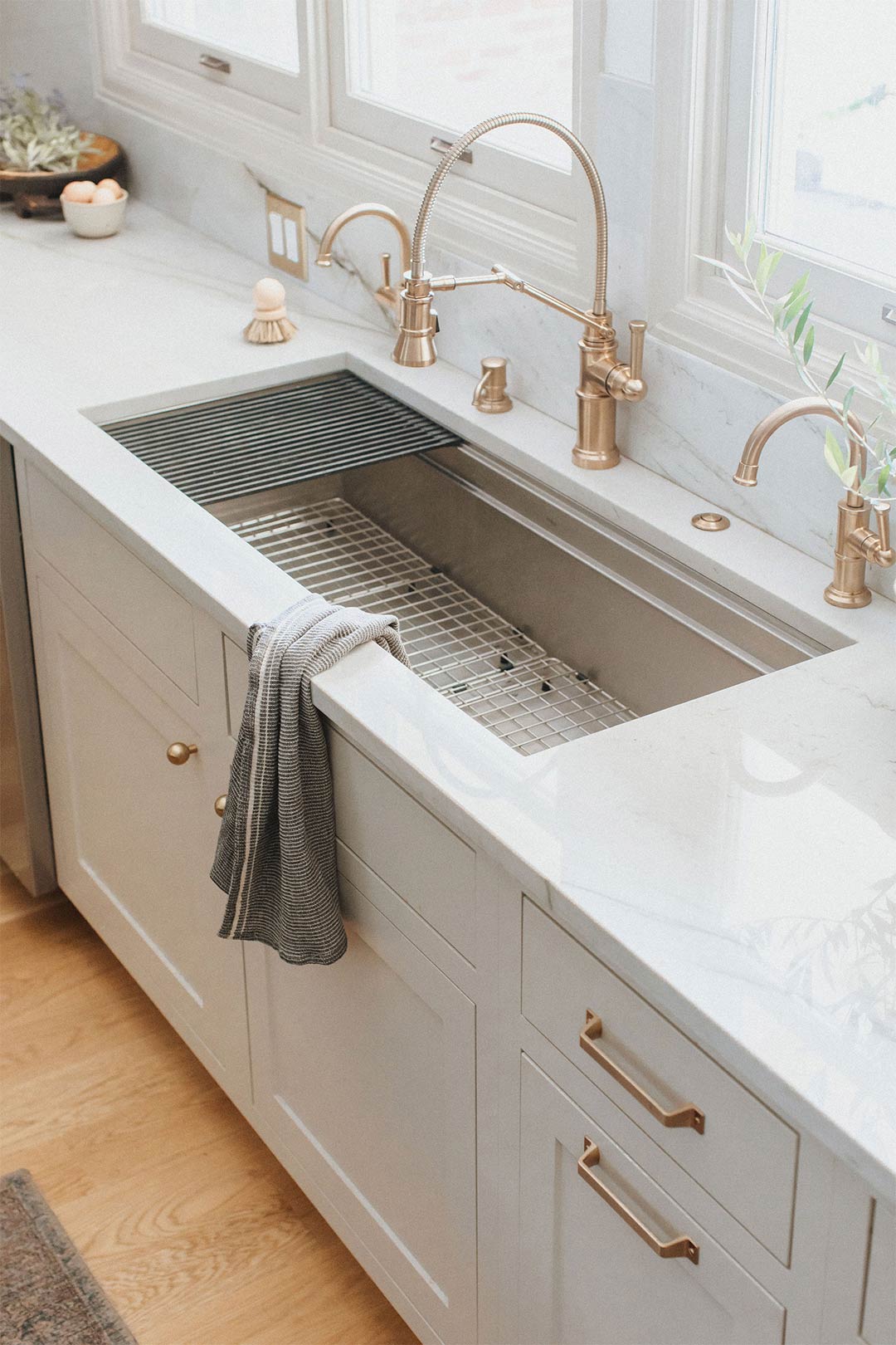 Brizo Artesso Faucets in Luxe Gold paired with a Stainless Steel Workstation Sink from Elkay Crosstown with Quartzite countertops and a slab backsplash.