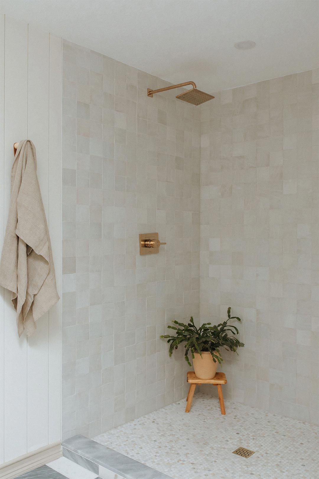 Zagora 2" x 2" Zellige Wall Tile - in a walk in shower with brass faucet and a Vintage Wood Milking Stool with a plant in the shower styled by Jennifer Murphy of J. Reiko Design + Co
