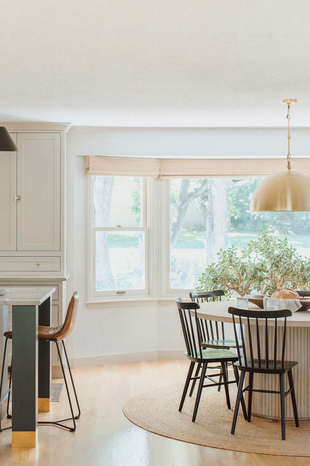 View of the dining nook next to the navy island in a Modern European farmhouse kitchen in front of  Woven Roman Shades 