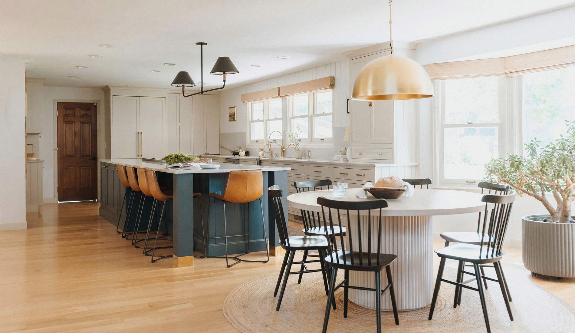 An open concept Modern European Farmhouse kitchen with a dining nook with black farmhouse chairs and a domed brass pendant light