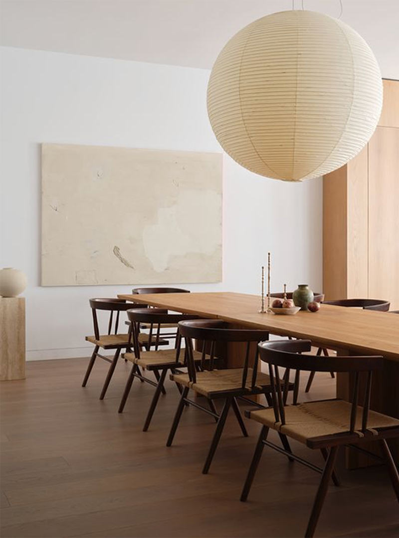 Japandi dining room with an oversized paper lantern chandelier and a natural wood tone table with woven seat wishbone back chairs from a project by Christina Cole and Co