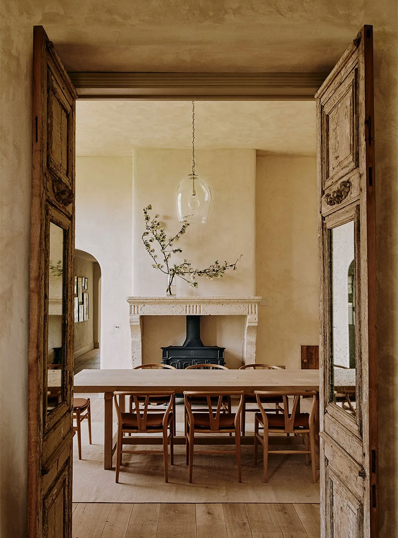 A Japandi dining room with natural wood wishbone back chairs and a neutral toned stone mantel with minimal decor - design by Joanna Vesty