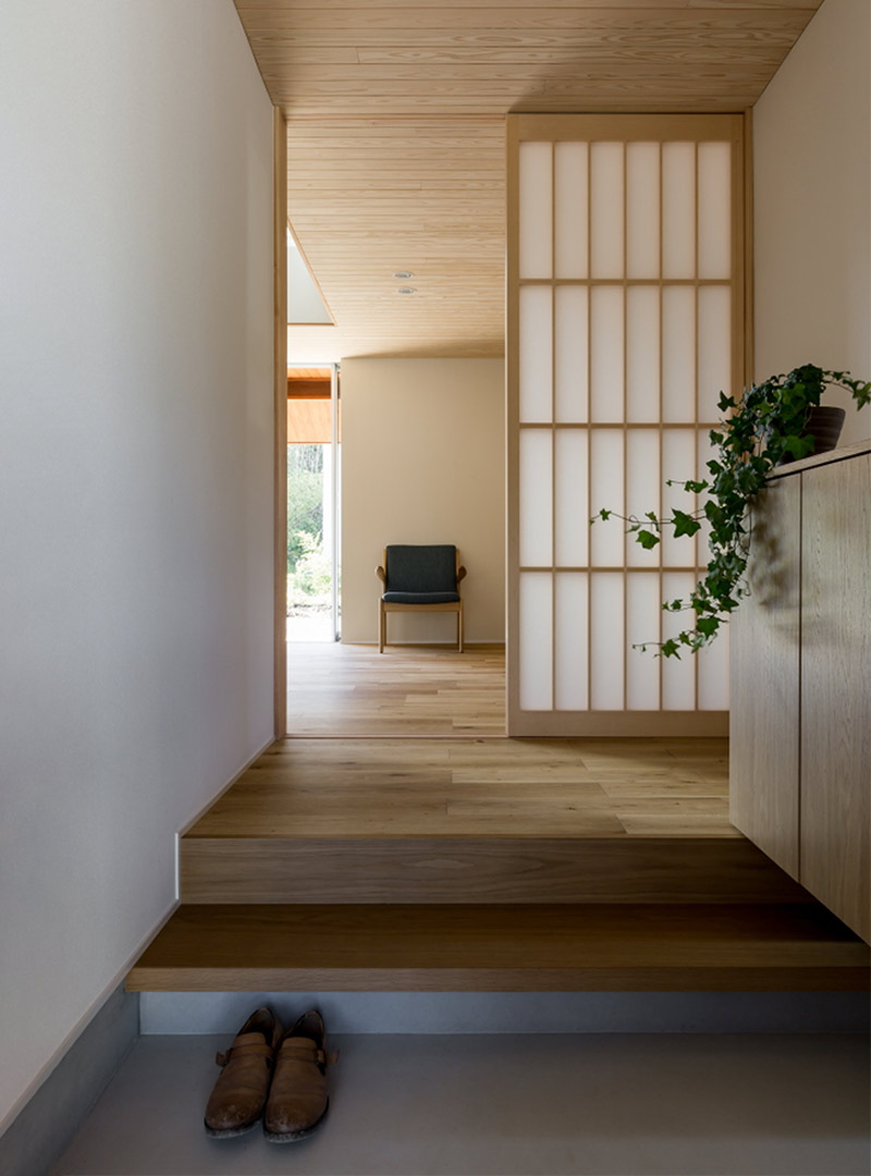 A minimal Japandi entryway from a project by Norm Architects with a neutral toned sliding screen and natural wood storage for shoes.