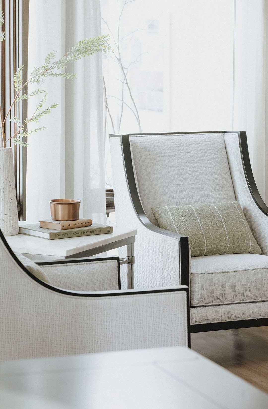 Two traditional white linen accent chairs with dark wood make a conversation area by the windows overlooking the Eagle Ranch Estate's lake.