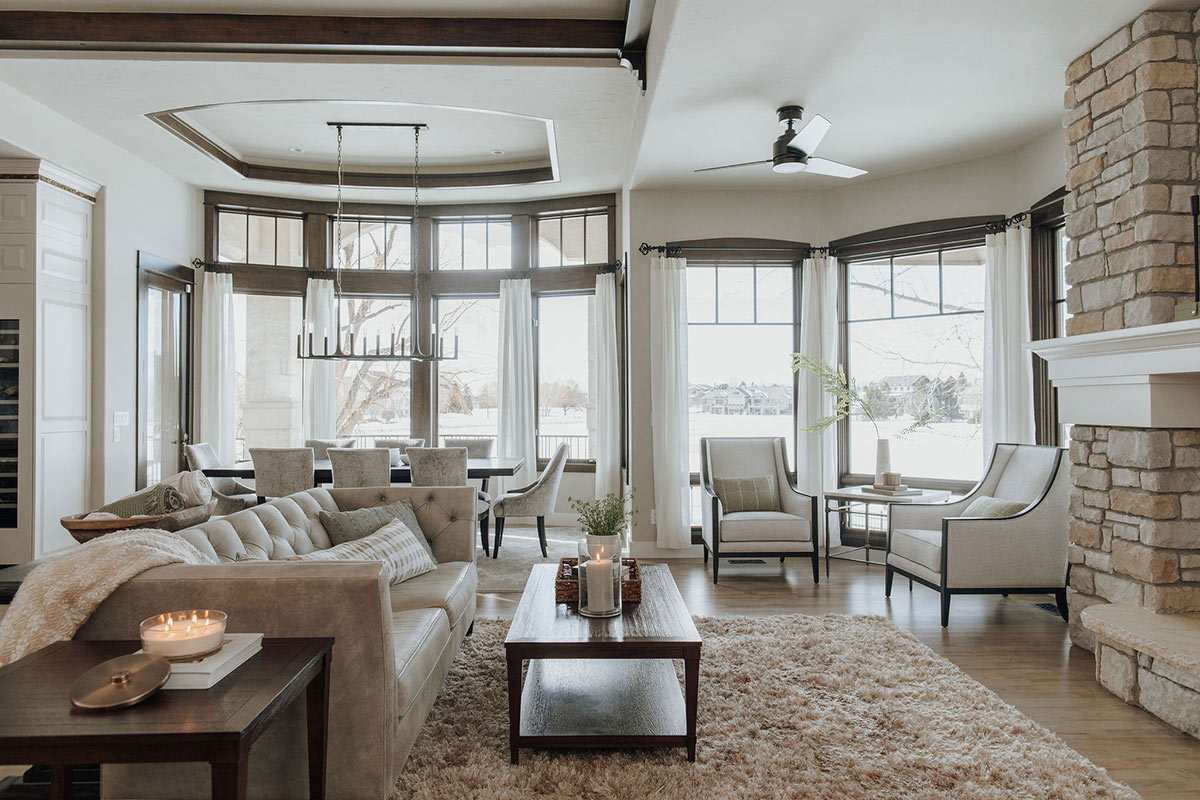 A neutral toned traditional, Mediterranean living room with dark wood trim, stone fireplace, and a Rejuvenation Petrel LED Ceiling Fan.