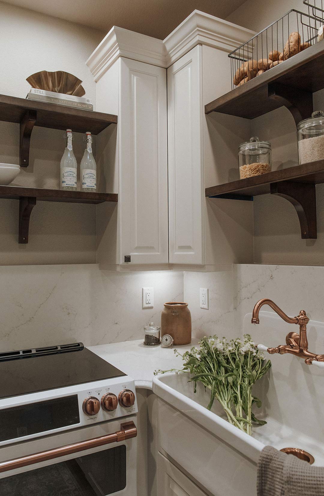 Café 30" Smart Slide-In, Front-Control, Induction and Convection Double-Oven Range is paired with open, dark wood shelving, white cabinets and a copper sink.