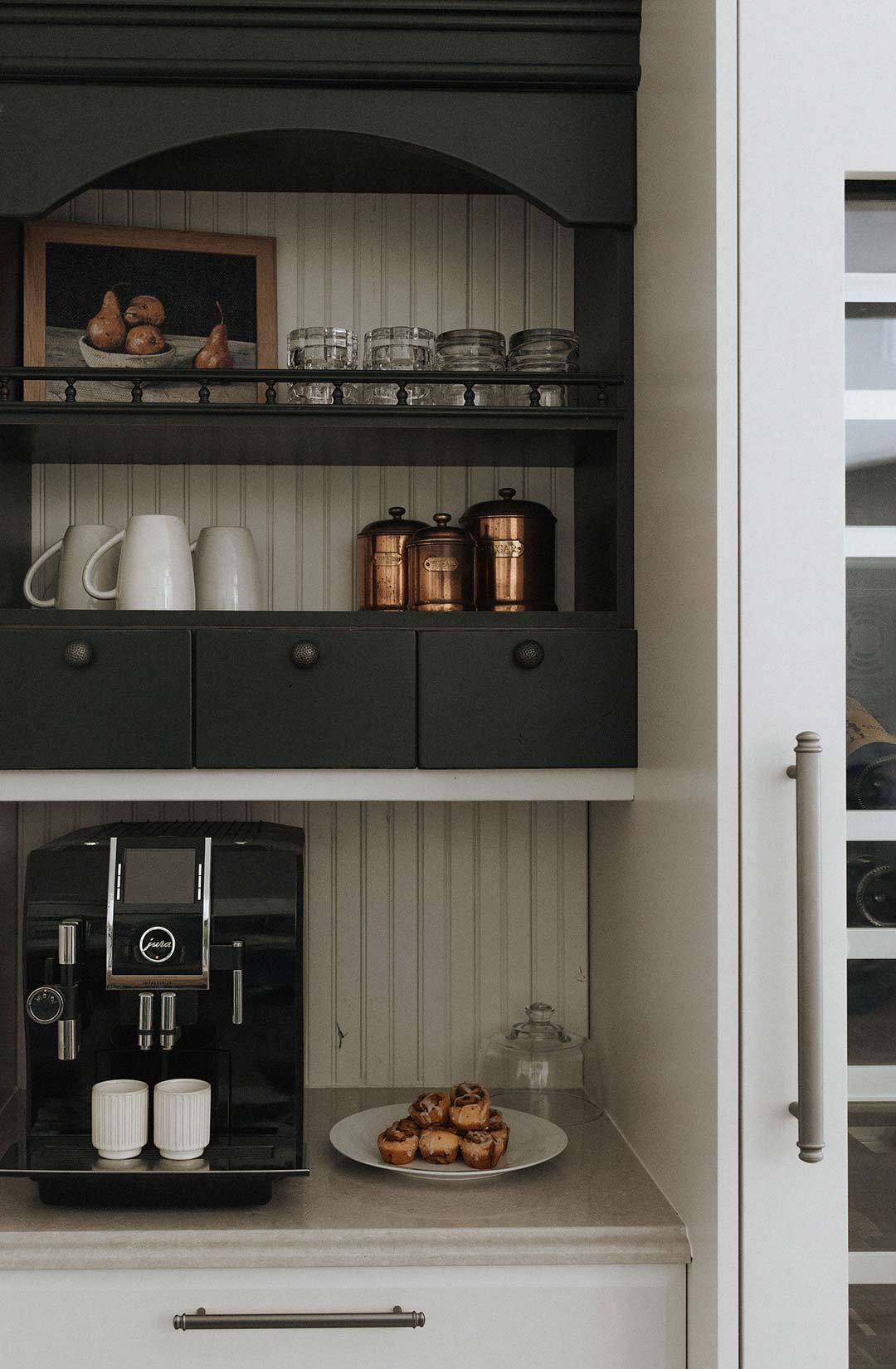 A coffee bar in a traditional kitchen features a dark wood cabinet with open shelves and three pull out drawers that is next to the Wine Tower - Wine Refrigerator