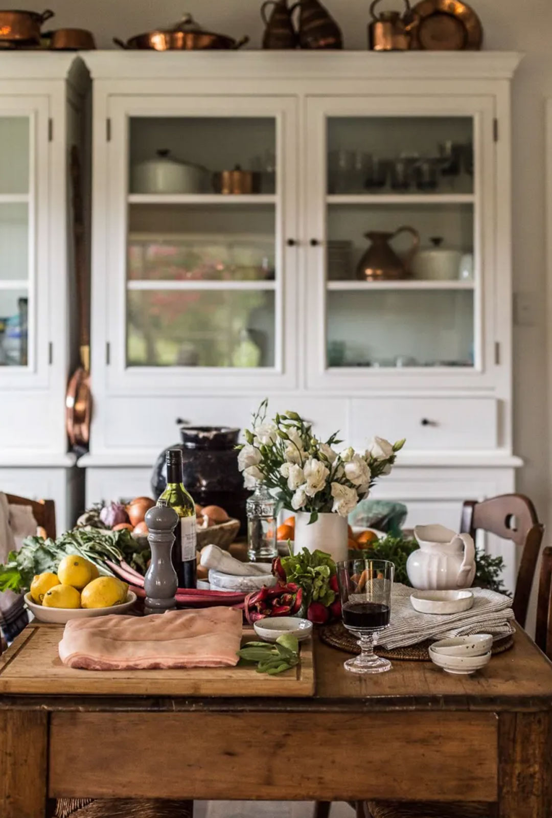 J. Reiko Design + Co - Bespoke English Kitchen - 05 An English country style table with fresh fruits and veggies and white shaker cabinets in the background show the handmade elements that speak to the bespoke nature of English design