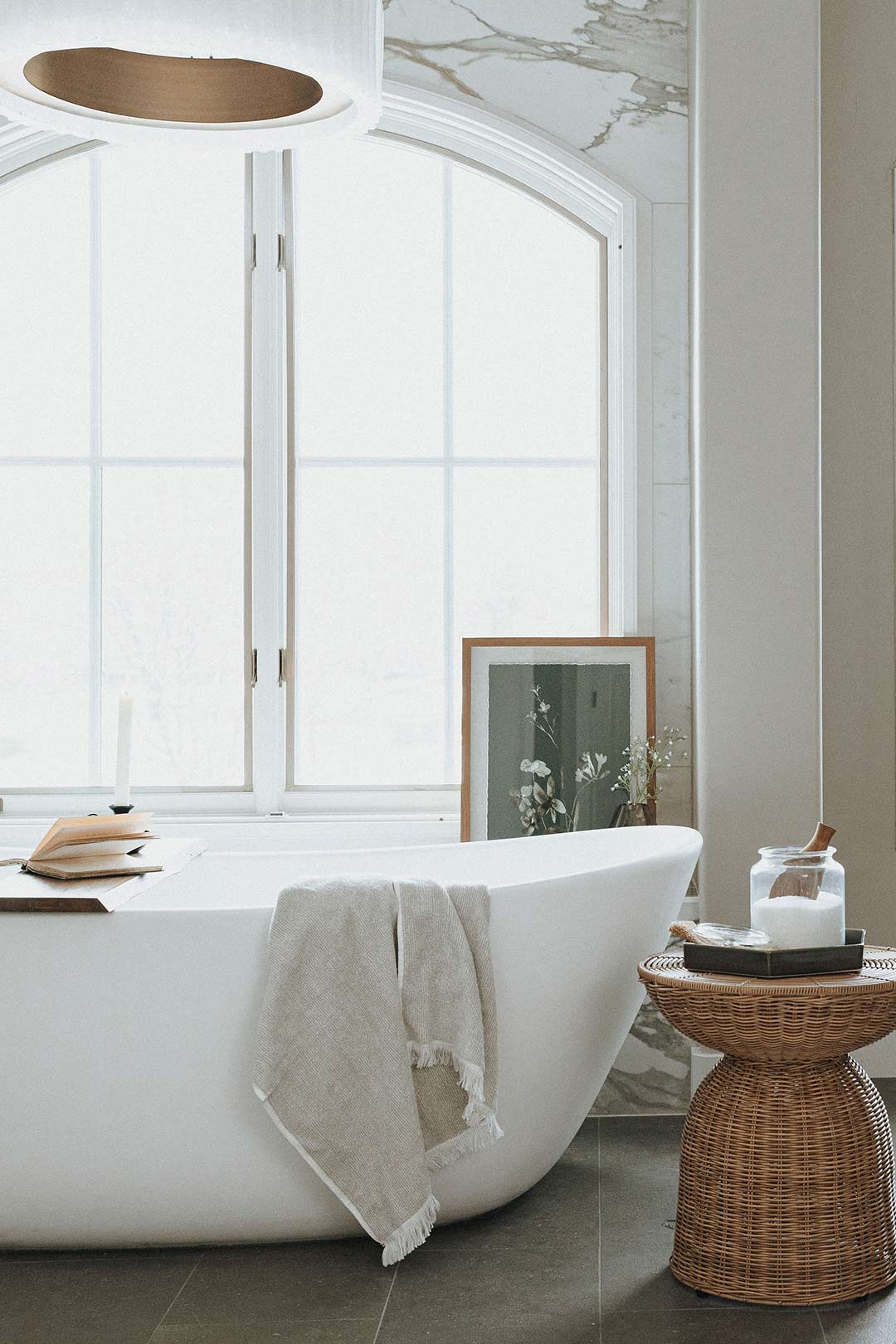 A free standing tub with floor to ceiling marble accent wall and contemporary light fixture with rustic styling by Jenny Murphy of J. Reiko Design + Co