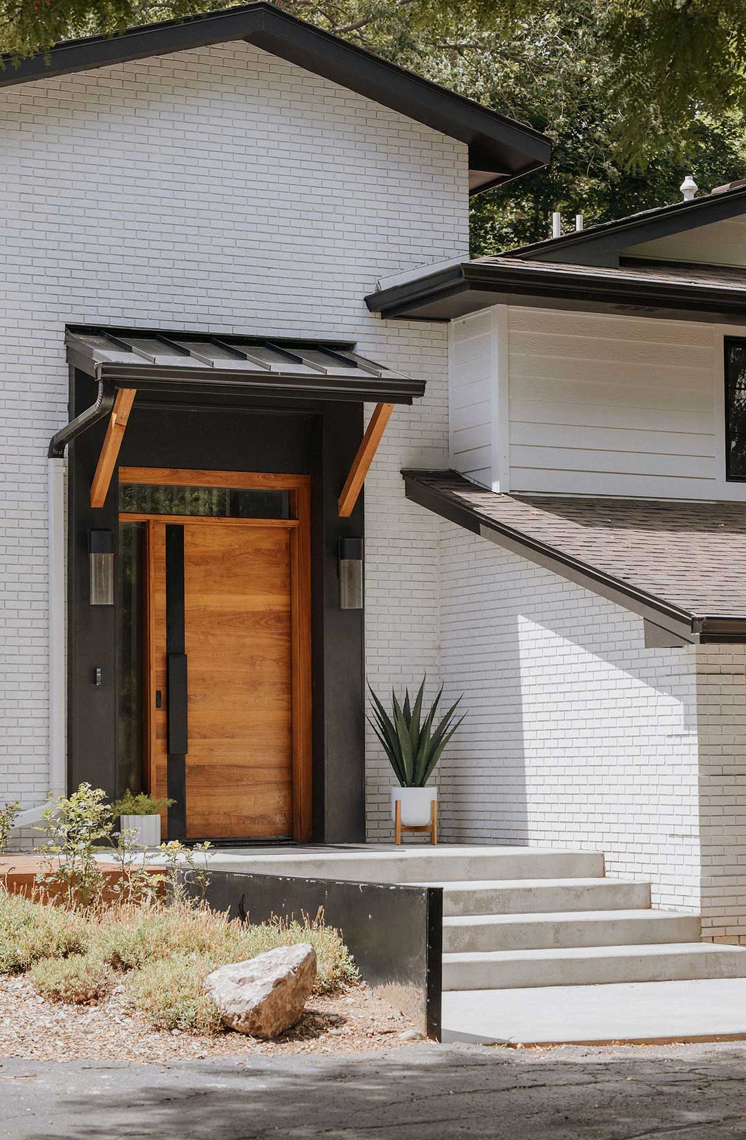 Front entry and exterior design of a mid-century remodel in Northern Colorado. The oversized front door is made from horizontal cedar wood slats, framing the door are Hinkley Shelter outdoor wall sconces.