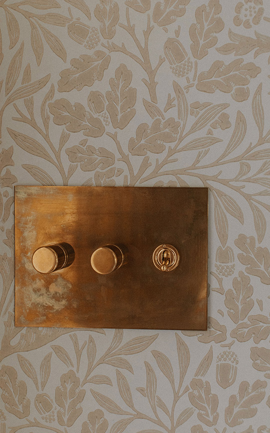 J. Reiko Design + Co. - Selecting Finishes - 10 Custom brass light switch in a historic home on a decorative wallpaper.