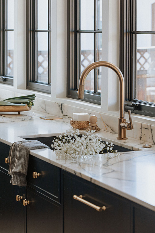 J. Reiko Design + Co. - Selecting Finishes - 5 A classic kitchen sink is shown with beautiful champagne bronze hardwear and kitchen cabinet pulls and knobs. A towel is draped over the counter and a bunch of baby's breath sits in the sink. Styling and design by J. Reiko Design + Co.