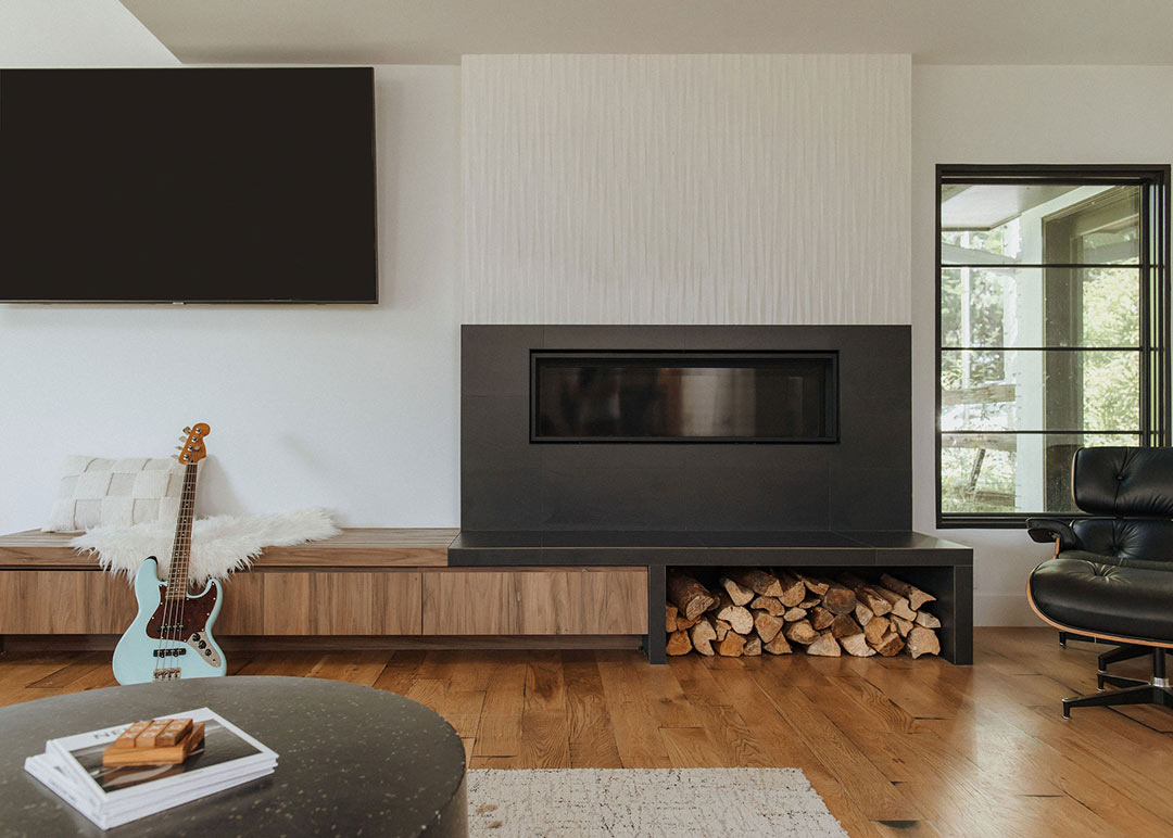 J. Reiko Design + Co. - Asymmetrical Rooms - 15 Sunlit living room with a built in bench under a mounted TV and a modern black fireplace balanced by seating arrangement, offset window, and natural materials.