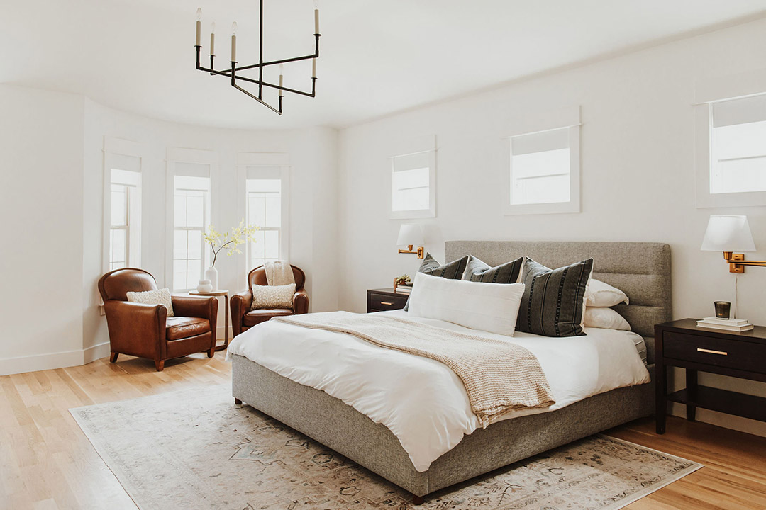 J. Reiko Design + Co. - Asymmetrical Rooms - 03 Bright bedroom with a centered upholstered bed balanced by off-set leather chairs, layered rugs, and varied window placement.